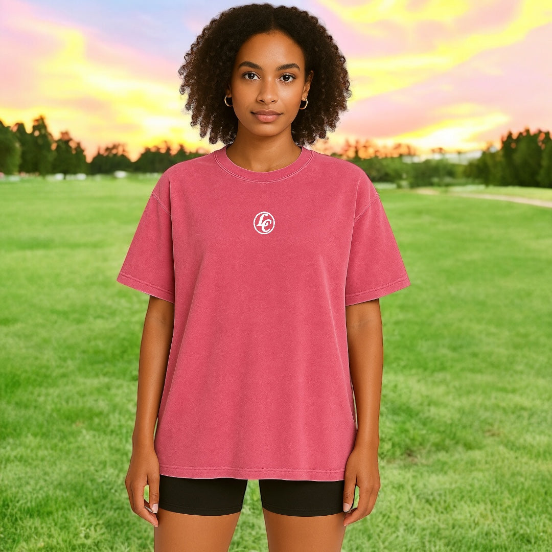 Person wearing a pink t-shirt with a logo in a park setting