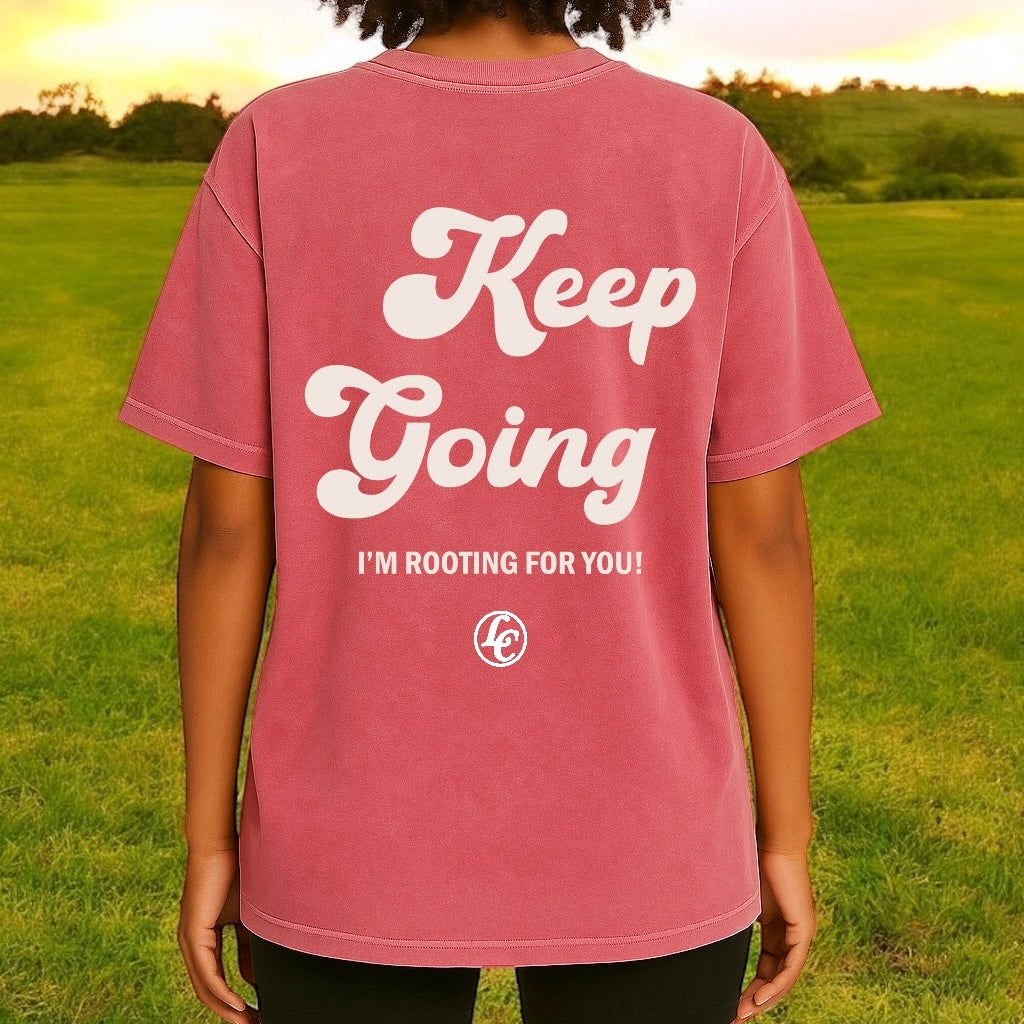 Person wearing a pink t-shirt with 'Keep Going' text in a field