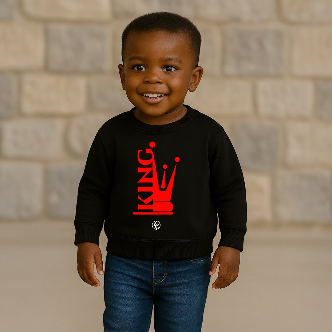 Child wearing a black sweatshirt with a red 'KING' graphic against a brick wall background