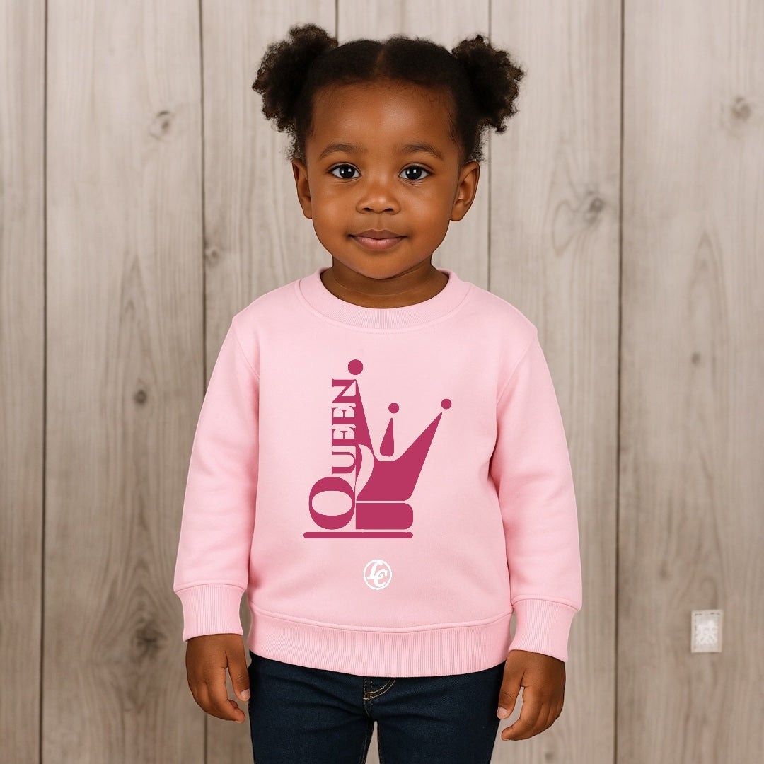 Child wearing a pink sweatshirt with 'Queen' design against a wooden background