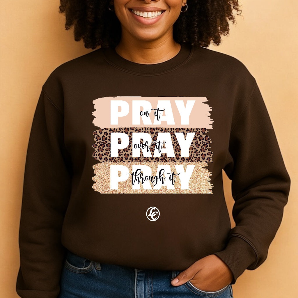 Person wearing a brown sweatshirt with 'PRAY on it, PRAY over it, PRAY through it' text design.