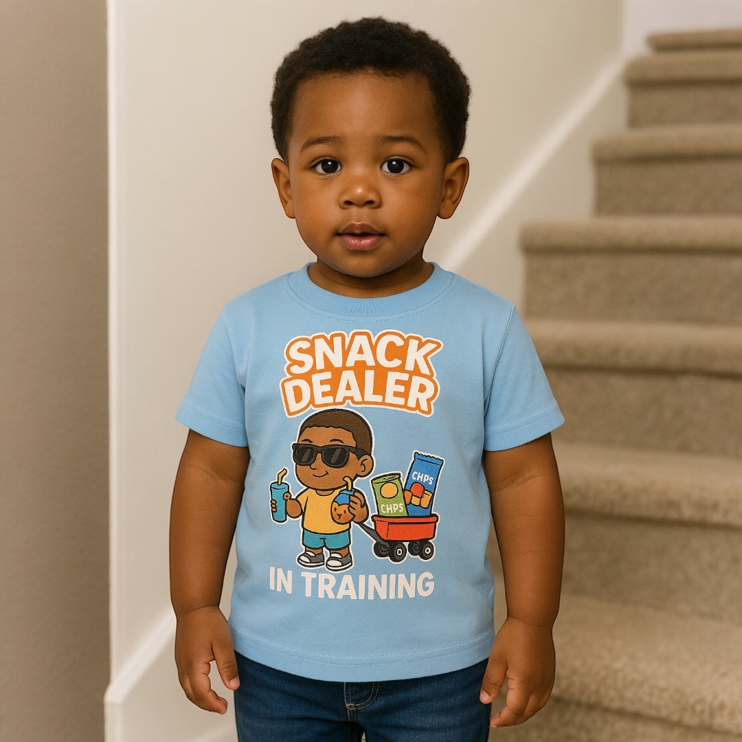 Child wearing a blue t-shirt with 'Snack Dealer In Training' text and graphics.