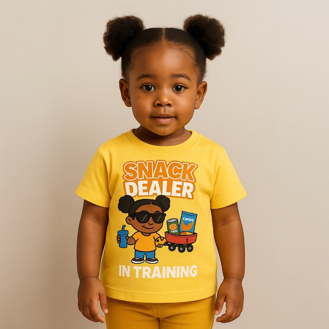 Child wearing a yellow t-shirt with 'Snack Dealer In Training' text and graphics on a beige background