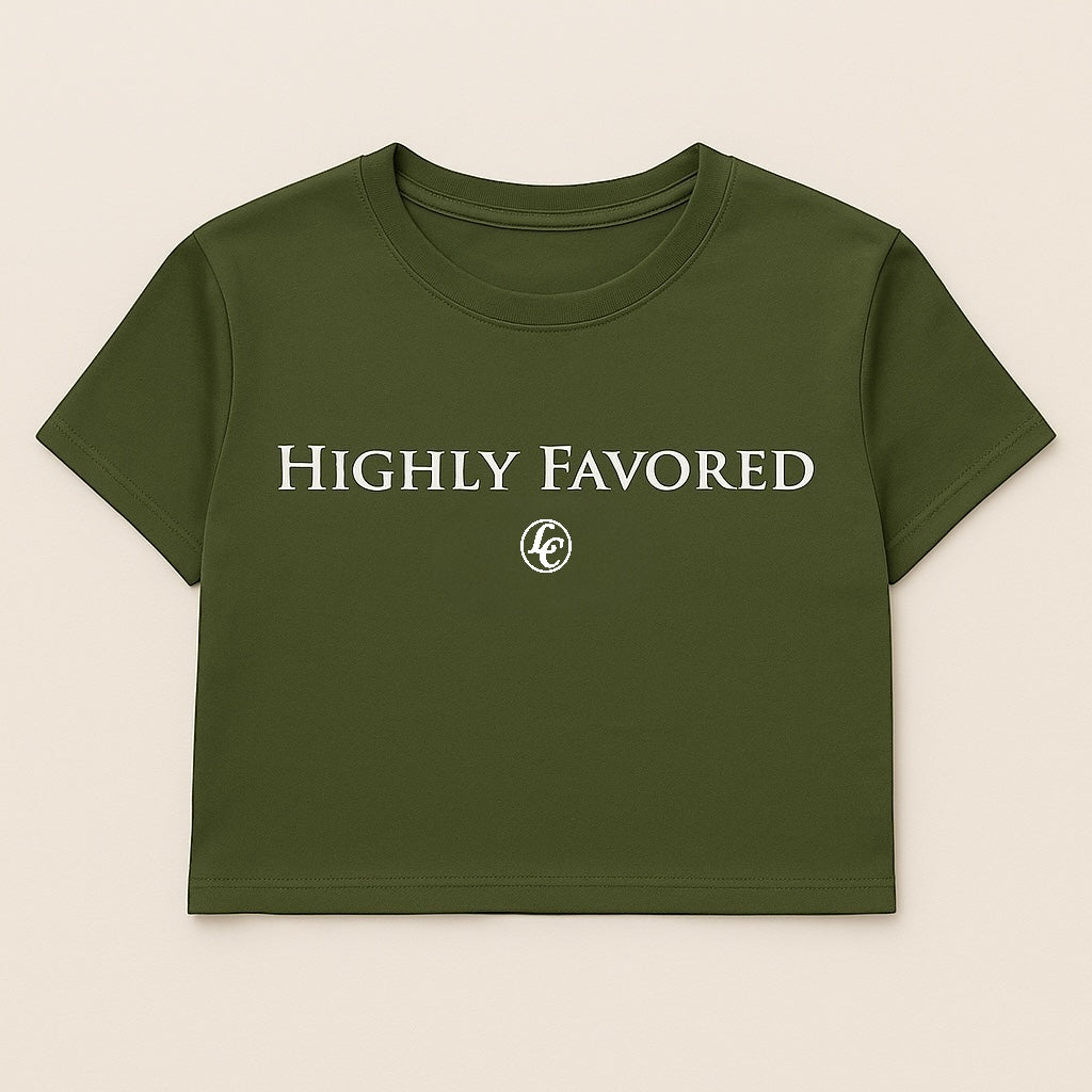 Green crop top t-shirt with 'HIGHLY FAVORED' text on a beige background